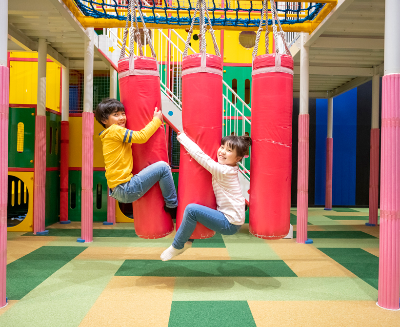 アスレチックゾーンの柔らかいブロックに抱きついて笑顔でぶら下がっている子どもたち